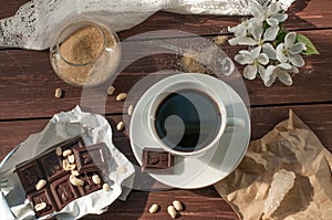 A composition with a cup of coffee, a chocolate bar and a blooming twig of an apple tree