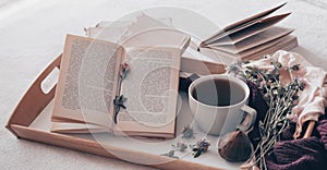 Composition of a cup of tea and opened book is not readable on a coffee table in the room, with figs and flowers. close up