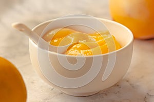 Composition with delicious Yellow lemons and Lemon curd in a sausepan white bowl on marble background