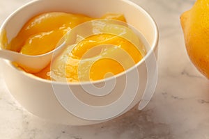 Composition with delicious Yellow lemons and Lemon curd in a sausepan white bowl on marble background