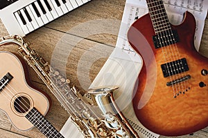 Composition of different musical instruments: synthesizer, electronic guitar, saxophone and ukulele lying, sheets with