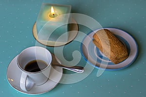 Composition with espresso cup, saucer with biscuits and lit candle with predominance of white and light blue colors photo