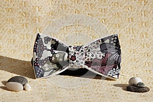 Composition: Extravagant bow tie and pebbles on a beige background.