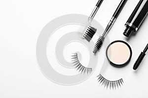 Composition with false eyelashes and other makeup products on white background