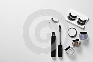 Composition with false eyelashes and other makeup products on white background, top