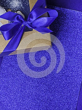 Composition of festive gift wrapped present box with blue satin bow on trendy blue background, copy space