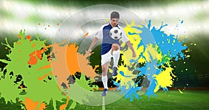 Composition of football player kicking ball over splodges and sports stadium background