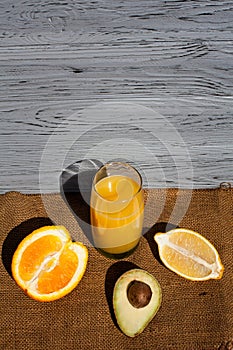 Composition of fresh fruits, orange, avocado halves and lemon, lying around orange juice in a glass