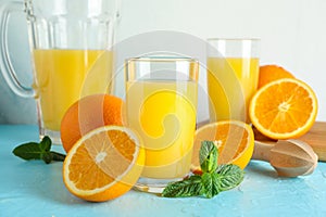 Composition with fresh orange juice in glassware, mint and wooden juicer on color table against white background, closeup