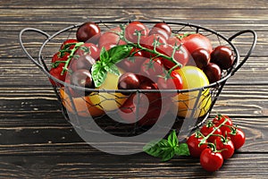 Composition of fresh ripe tomatoes of different varieties, spices, basil, rosemary, thyme, hot pepper in a basket on a wooden boar