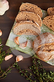 Composition of garlic and bread on a dark wooden table. Freshly baked hand-made bread on a kitchen towel. Bread is cut into slices