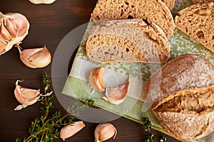 Composition of garlic and bread on a dark wooden table. Freshly baked hand-made bread on a kitchen towel. Bread is cut into slices