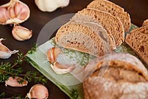 Composition of garlic and bread on a dark wooden table. Freshly baked hand-made bread on a kitchen towel. Bread is cut into slices