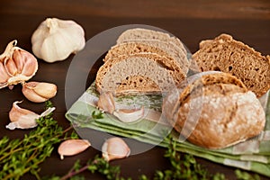 Composition of garlic and bread on a dark wooden table. Freshly baked hand-made bread on a kitchen towel. Bread is cut into slices