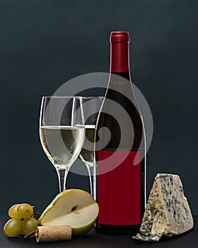 Composition with glass and bottle of white wine with blue mold cheese, pear and grapes on grey background. copy space