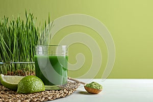 Composition with glass of wheat grass juice and lime on table against green background