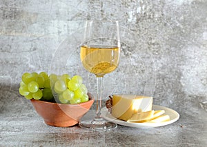 Composition of a glass of white wine cheese and a bunch of grapes on a plate photo