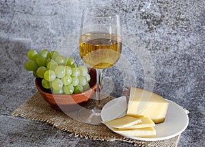 Composition of a glass of white wine cheese and a bunch of grapes on a plate photo