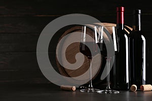 Composition with glasses and bottles of red wine on table against dark background
