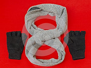 Composition of gray scarf and black gloves, both of wool, on a bright red background.