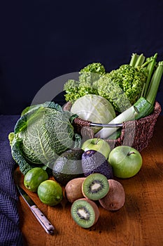 Composition of green vegetarian products on a dark background: green leafy vegetables, onions, avocados, kiwis, green apples,