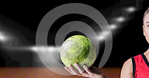 Composition of hand of female volleyball player holding ball over blurred indoor court background