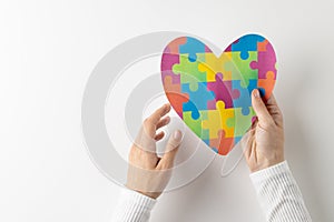 Composition of hands holding jigsaw puzzle heart on white background with copy space