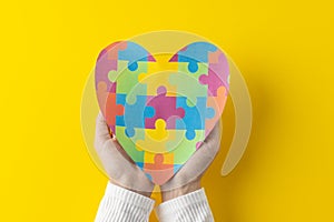 Composition of hands holding jigsaw puzzle heart on yellow background with copy space