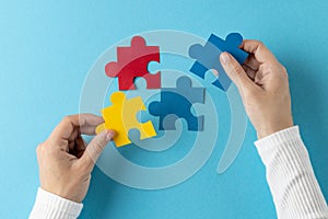 Composition of hands putting jigsaw puzzle pieces together on blue background with copy space