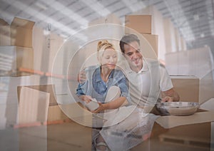 Composition of happy couple unpacking in new home over stacks of cardboard boxes in warehouse