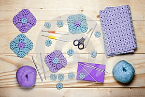 Composition of knitting accessories. Purple crocheted square napkins, balls of wool yarn, scissors, crochet hooks on light