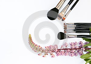 Composition with makeup cosmetics, brushes, and flowers on white background