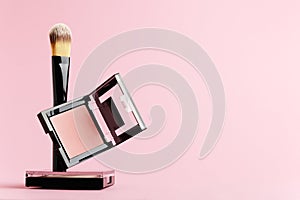 Composition with makeup items on a white background. Black brush, makeup tool, packing of rouge and powder levitate on a pastel