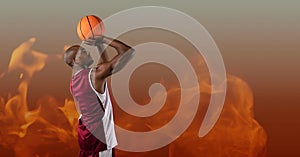 Composition of male basketball player shooting ball, over flames on grey background