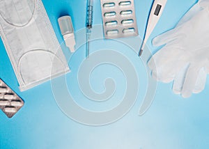 Composition with medical mask, thermometer, syringe, pills and gloves on a blue background.
