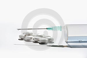 Composition with a medical syringe and several pills on a white background