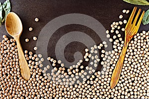 Composition of natural chickpeas with kitchen utensils, spoon and wooden fork on rustic textured bottom. View from above with