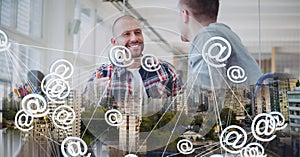 Composition of network of email icons over two businessmen talking in office