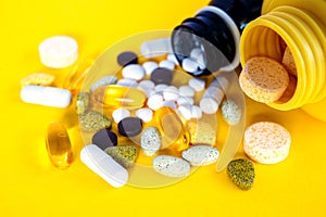 Composition with nutritional supplement capsules and containers. Variety of drug pills food supplement and vitamins on yellow back