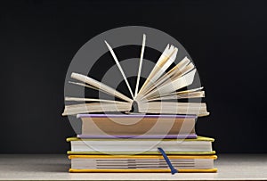 Composition with open book, hardback books on wooden table and black background. Back to school. Education background.