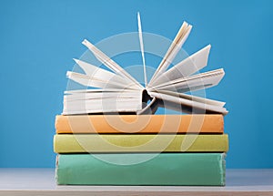 Composition with open book, hardback books on wooden table and blue background. Back to school. Education background.