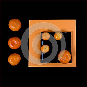 Composition of orange mandarin and black square plate on an orange table