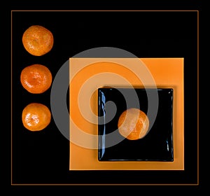 Composition of orange mandarin and black square plate on an orange table