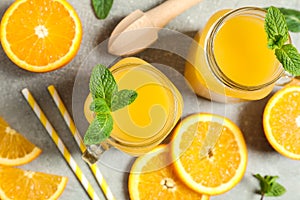 Composition with orange pieces, mint, tubules, wooden juicer and glass jars with fresh orange juice on grey background
