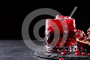 A composition of a organic pomegranate drink and cut garnet on a black background. Healthful and fresh red cocktails.