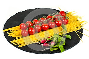 Composition of pasta fresh tomato, pepper, radish on black stone board, white background.