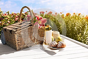 Composition with picnic basket and bottle of wine on wooden table in lily field. Space for text