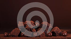 Composition of pieces of dark chocolate and round of chocolates in cocoa powder on brown background