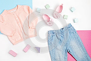 Composition with pink baby cardigan, jeans, and shoes on blue, pink and white background. Modern girly clothes