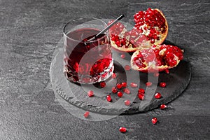 A composition of a pomegranate beverage and cut garnet on a dark gray background. Healthful, natural, fresh red juice.